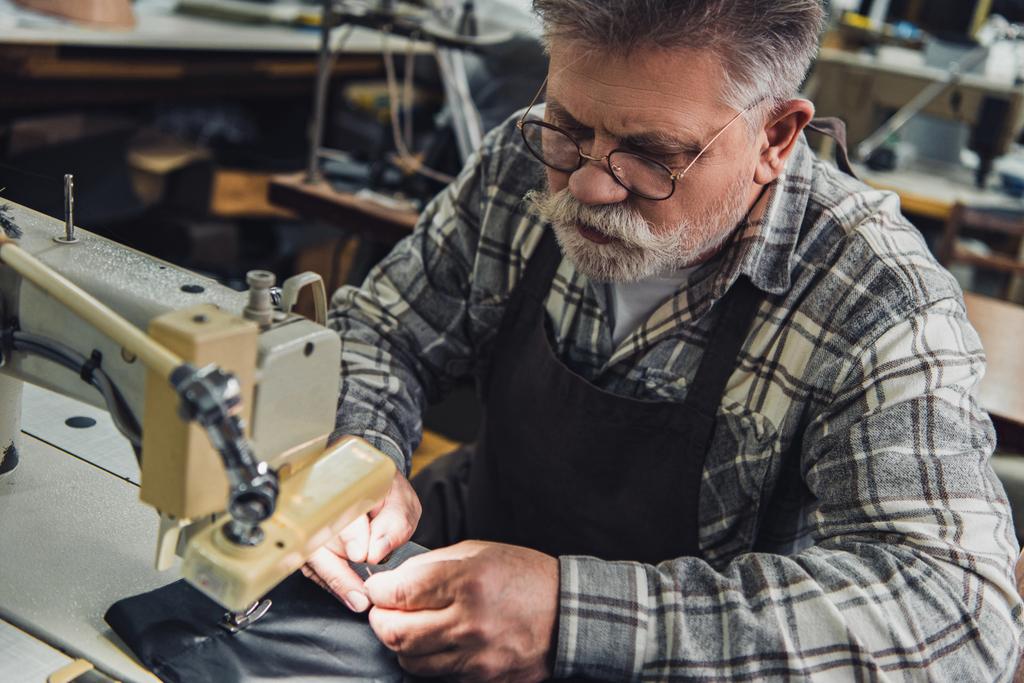 high angle view of male handbag craftsman working on sewing machine at studio - Photo, Image