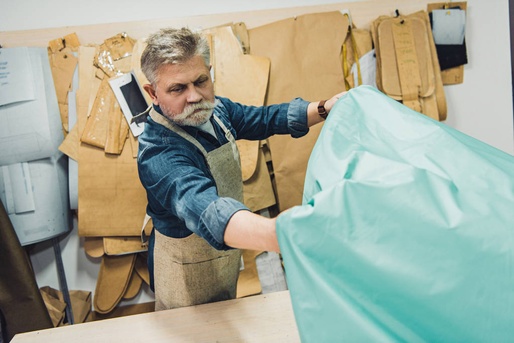 maturo artigiano borsa maschile mettendo tessuto sul tavolo di lavoro in studio
 - Foto, immagini