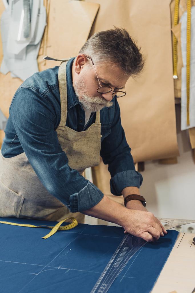 concentrato maschio di mezza età artigiano in grembiule fare misure su tessuto in officina
 - Foto, immagini