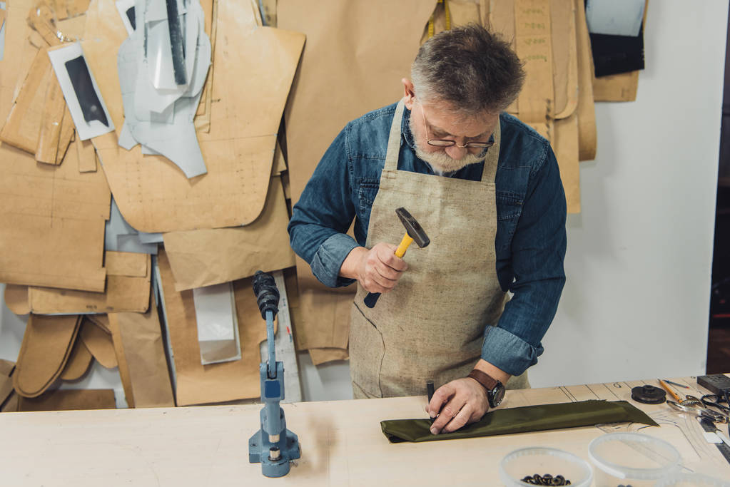 τεχνίτης εστιασμένη μέσης ηλικίας αρσενικό τσάντα εργασίας με σφυρί στο studio - Φωτογραφία, εικόνα