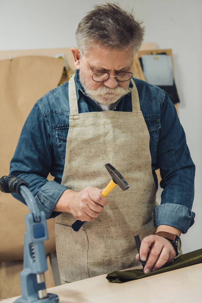 Männlicher Handtaschenhandwerker mittleren Alters arbeitet im Atelier mit Hammer - Foto, Bild