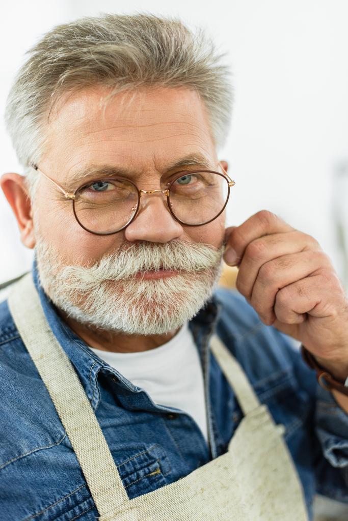 cheerful middle aged male craftsman in apron looking at camera in studio  - Photo, Image