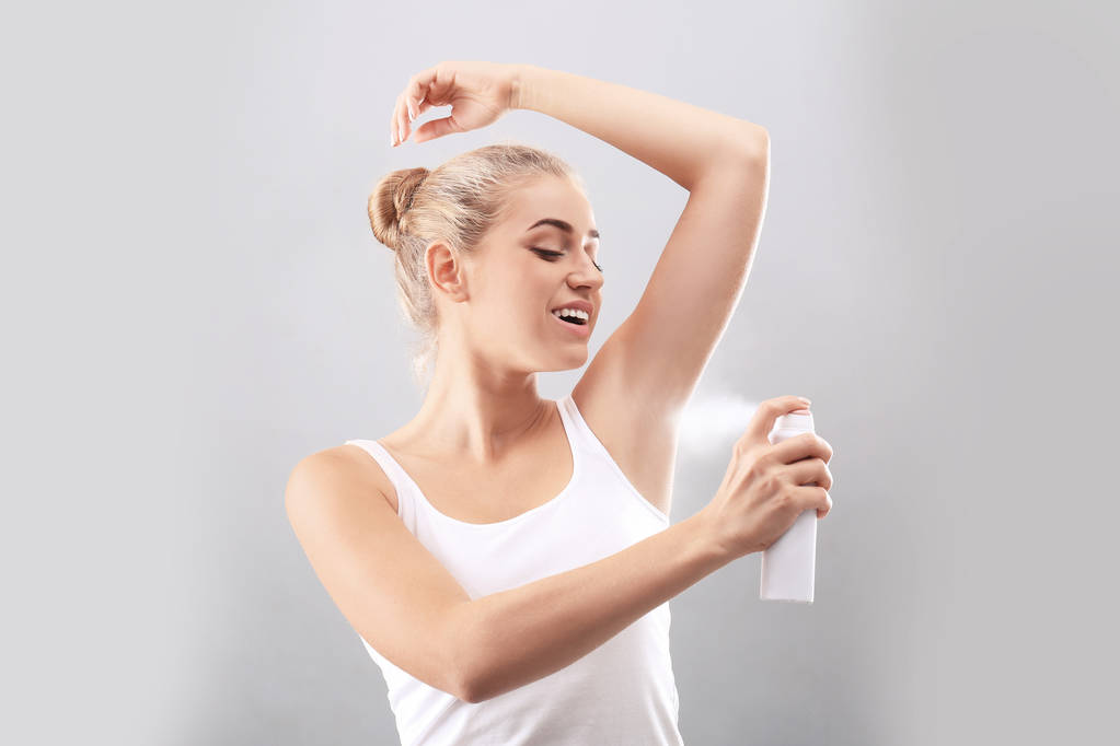 Молода жінка використовує дезодорант на сірому фоні
 - Фото, зображення