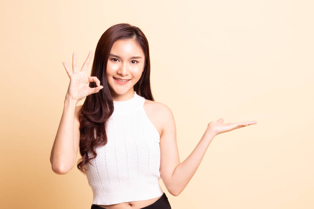 Belle jeune femme asiatique montrer la main de la paume et signe OK sur fond beige. - Photo, image