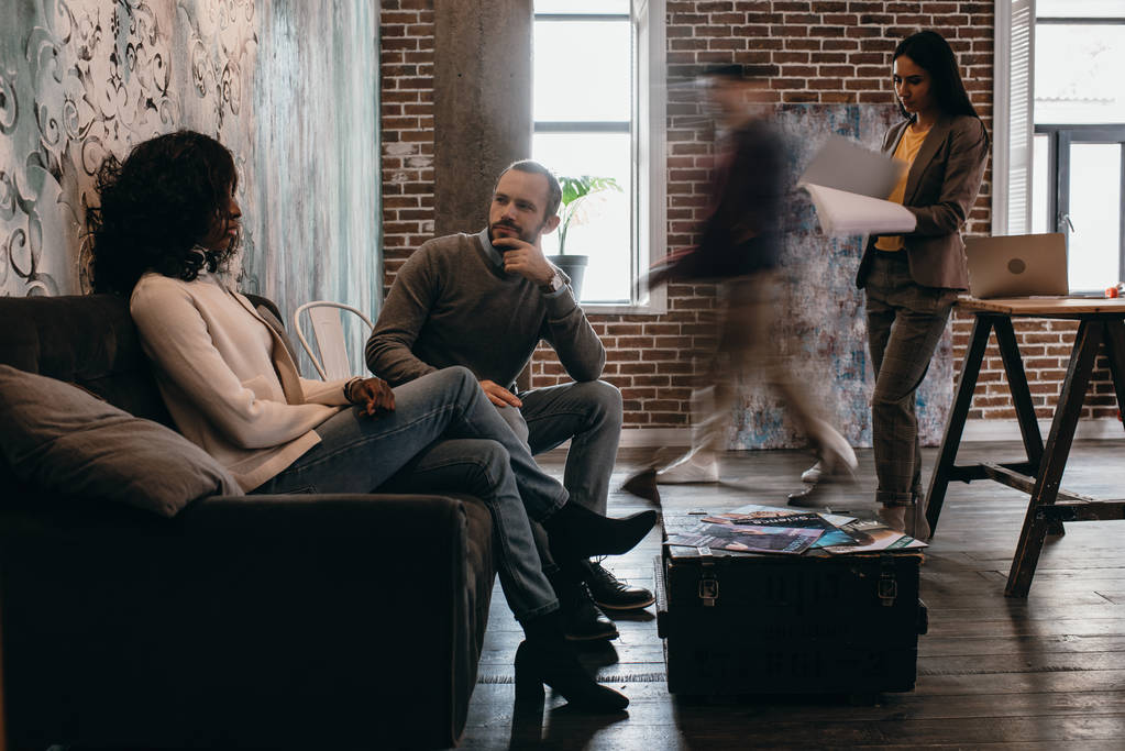 multikulturních pár ležérní podnikatelé sedí na gauči s kolegy v pohybu rozostření v kanceláři moderní loft - Fotografie, Obrázek