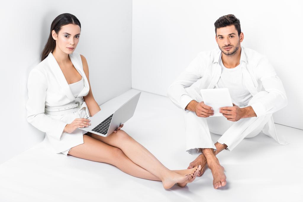 pareja de adultos en total blanco sentado en el suelo y el uso de dispositivos digitales
 - Foto, imagen