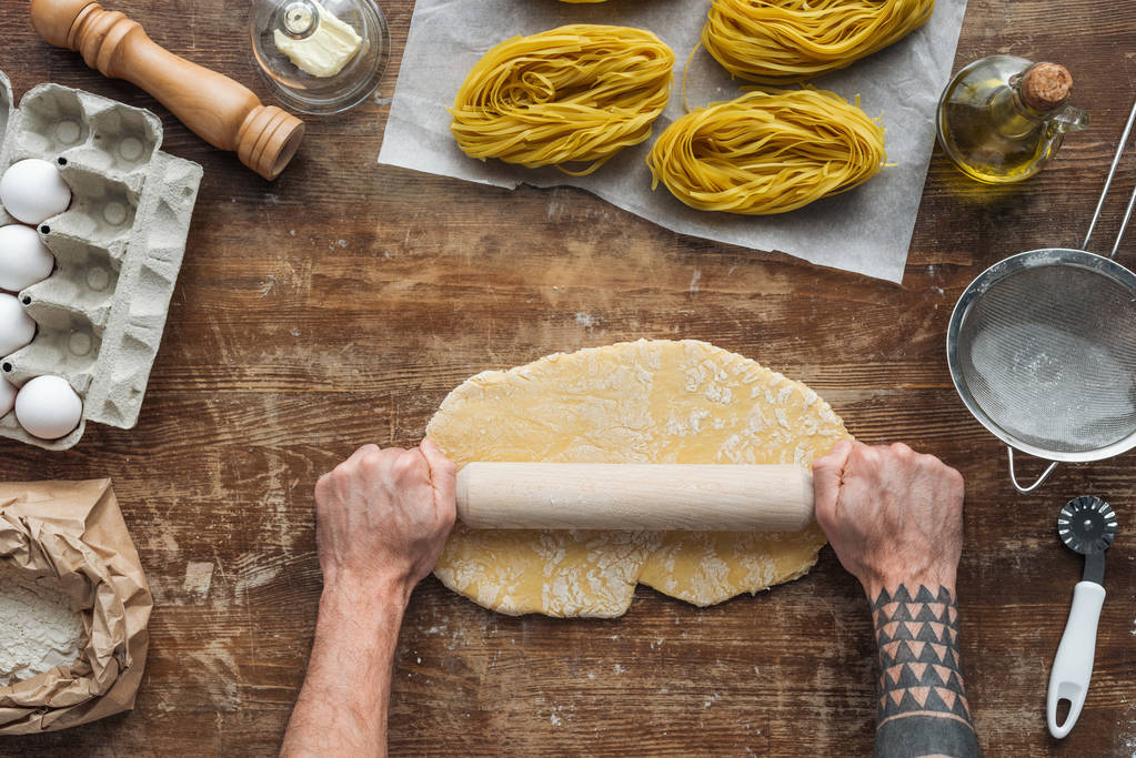 top view of male hands forming dough with rolling pin on wooden table - Photo, Image