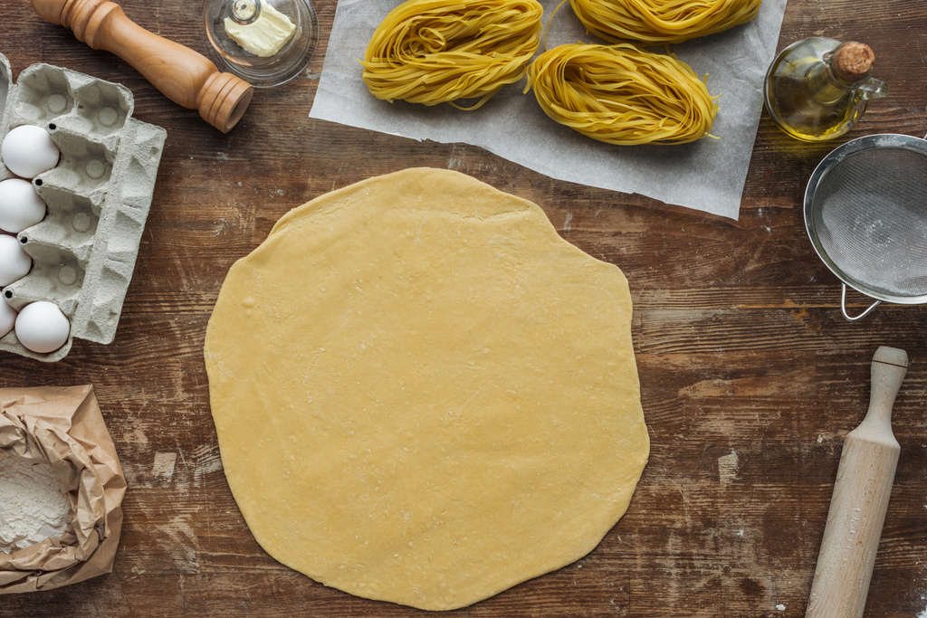 bovenaanzicht van opgerolde deeg voor de pasta op houten tafel - Foto, afbeelding