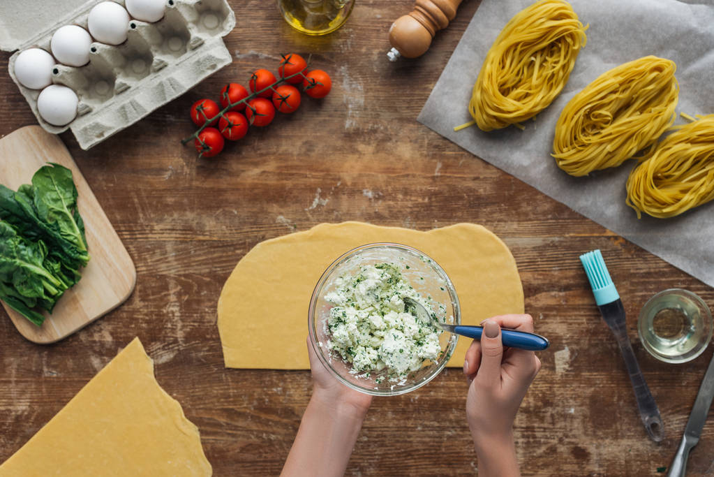 сверху вид женских рук, смешивающих шпинат и сливочный сыр с ложкой в миске на деревянном столе
 - Фото, изображение