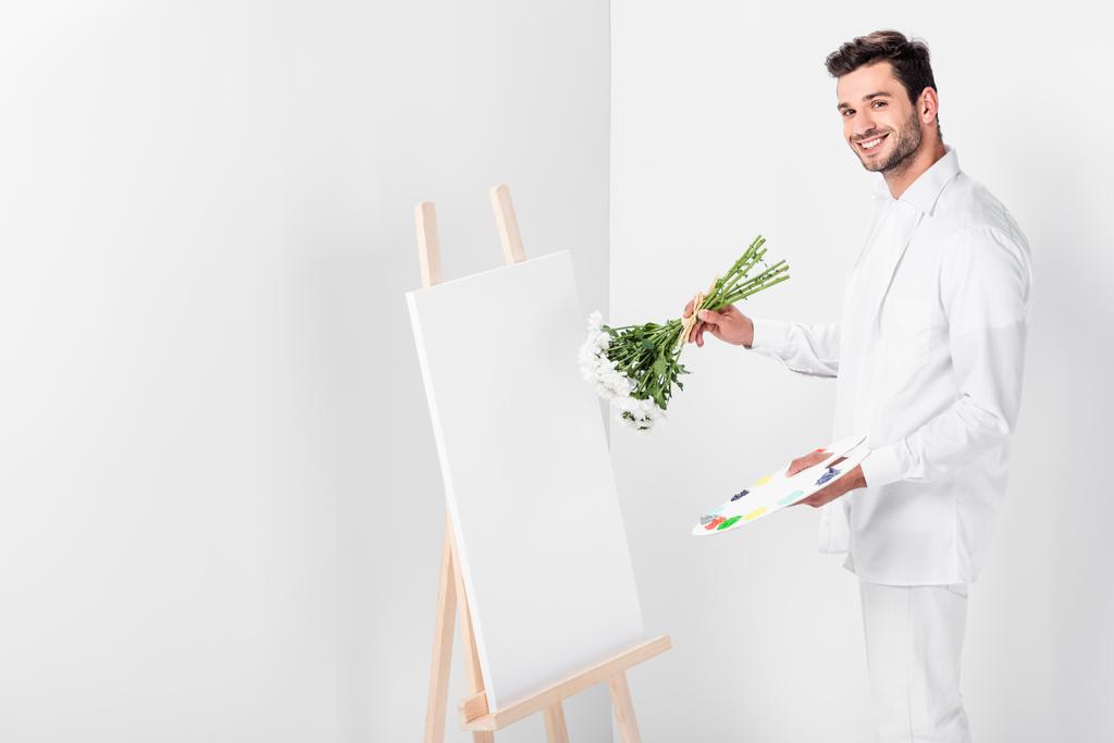 Крупный план художника-мужчины в целом белый рисунок на пустом мольберте с букетом цветов
 - Фото, изображение