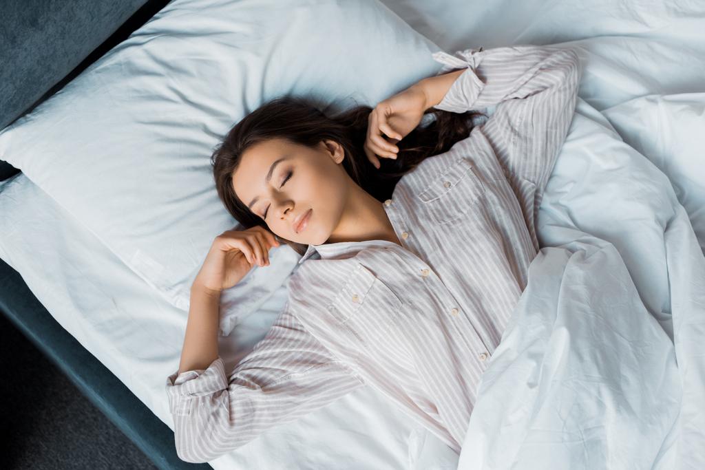 Top view of beautiful brunette woman in pajamas sleeping on bed in the morning
 - Фото, изображение