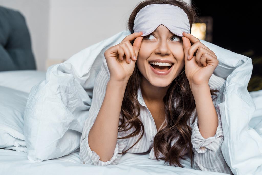 krásná vzrušená dívka v spací maska oční ležící v posteli - Fotografie, Obrázek
