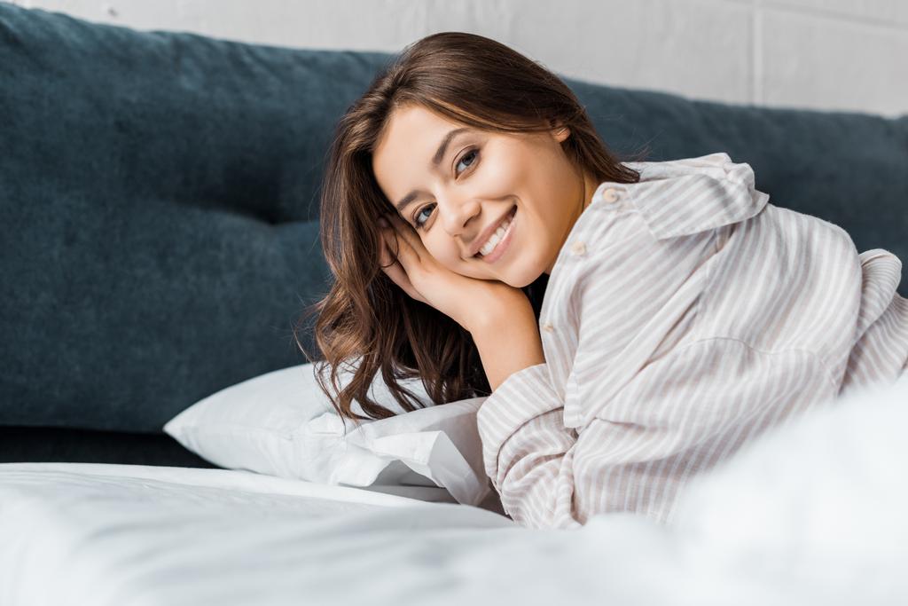χαμογελώντας τρυφερό κορίτσι με τις πυτζάμες ξαπλωμένη στο κρεβάτι - Φωτογραφία, εικόνα