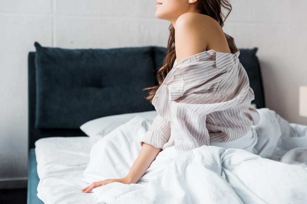 rajattu näkymä tarjouksen nainen pyjama istuu sängyllä aamulla
 - Valokuva, kuva