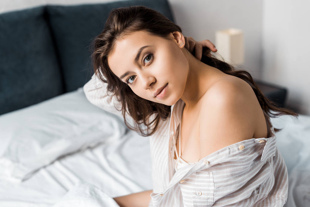 красивая нежная женщина, смотрящая в камеру и сидящая утром на кровати
 - Фото, изображение