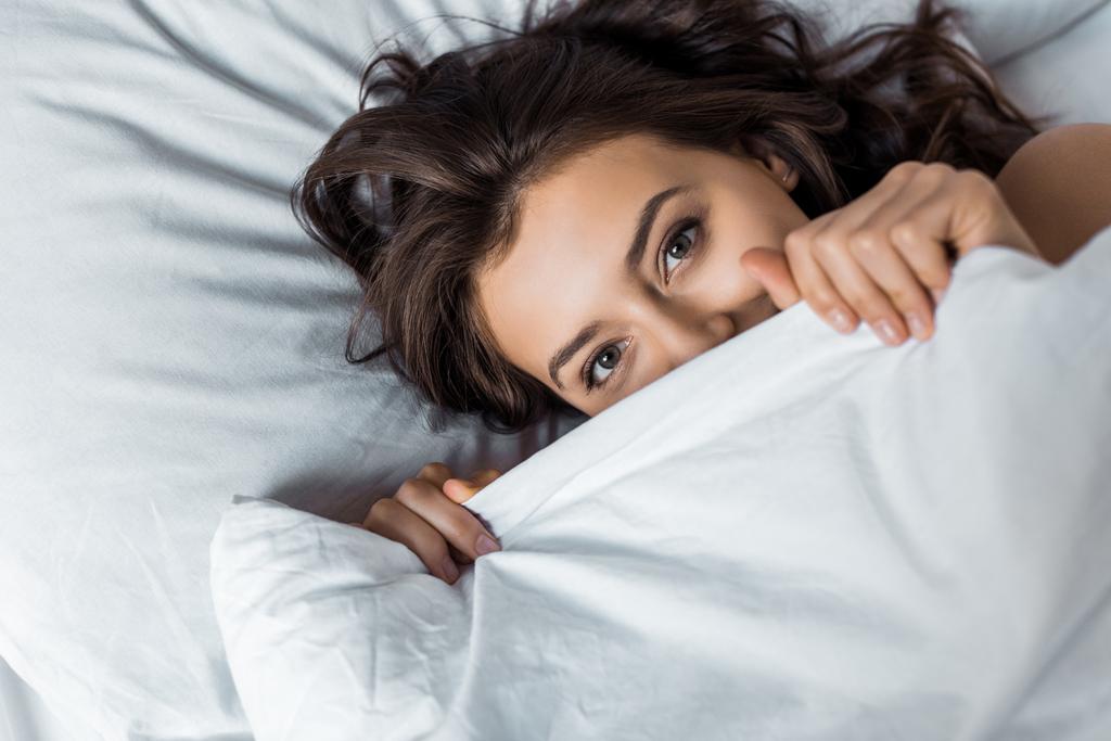 schöne glückliche Frau versteckt sich unter einer weißen Decke auf dem Bett - Foto, Bild