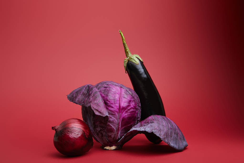 verse rijpe biologische UI, kool en aubergine op rode achtergrond  - Foto, afbeelding