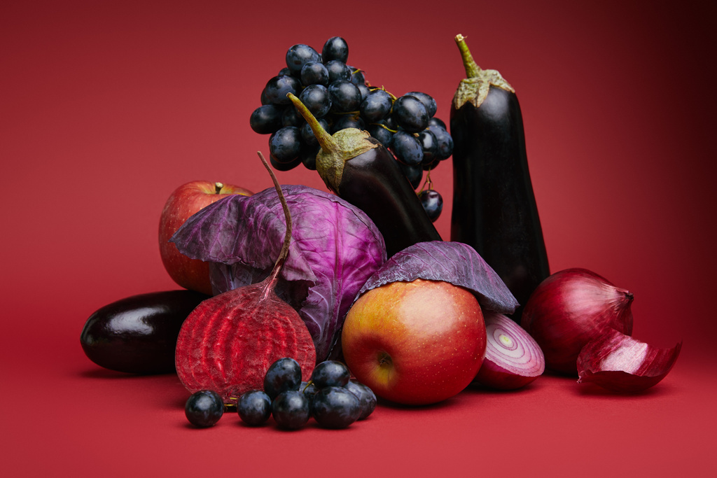 Vista de cerca de uvas frescas maduras, manzanas, berenjenas, remolacha, cebollas y repollo sobre rojo
 - Foto, Imagen