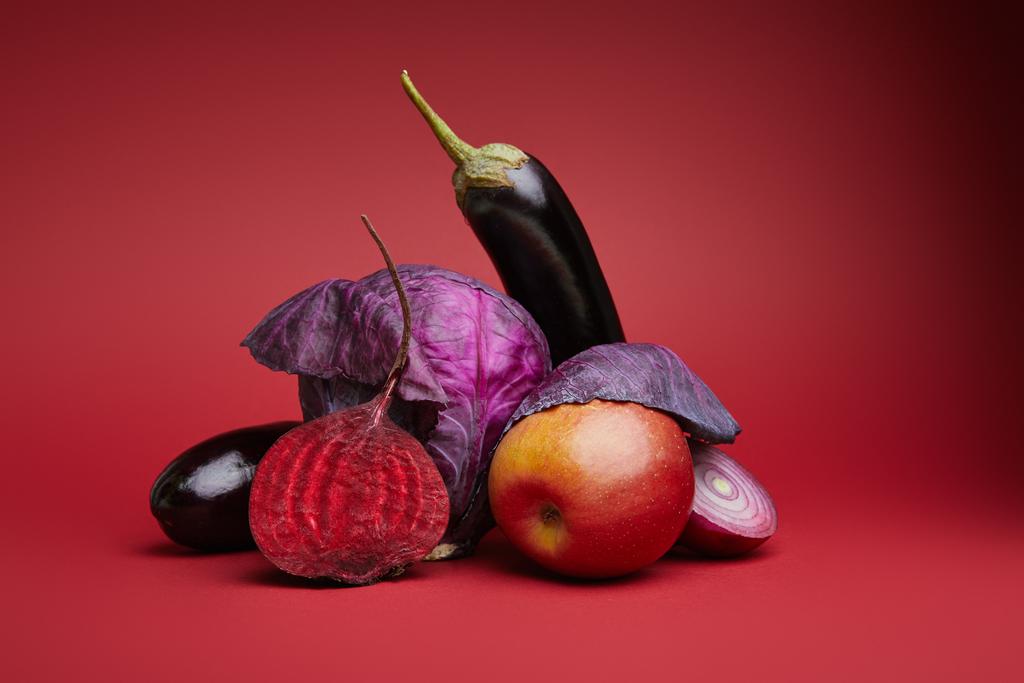 close-up view of ripe organic apple, cabbage, eggplants, onion and beetroot on red background - Photo, Image