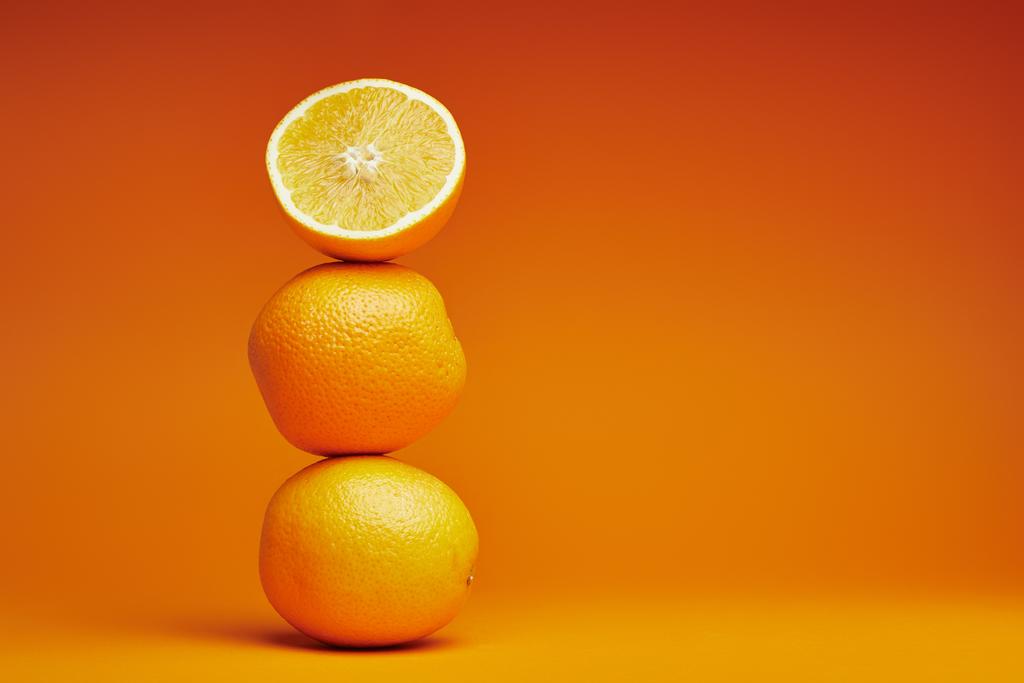 Крупный план цельных и нарезанных апельсинов на оранжевом фоне
  - Фото, изображение
