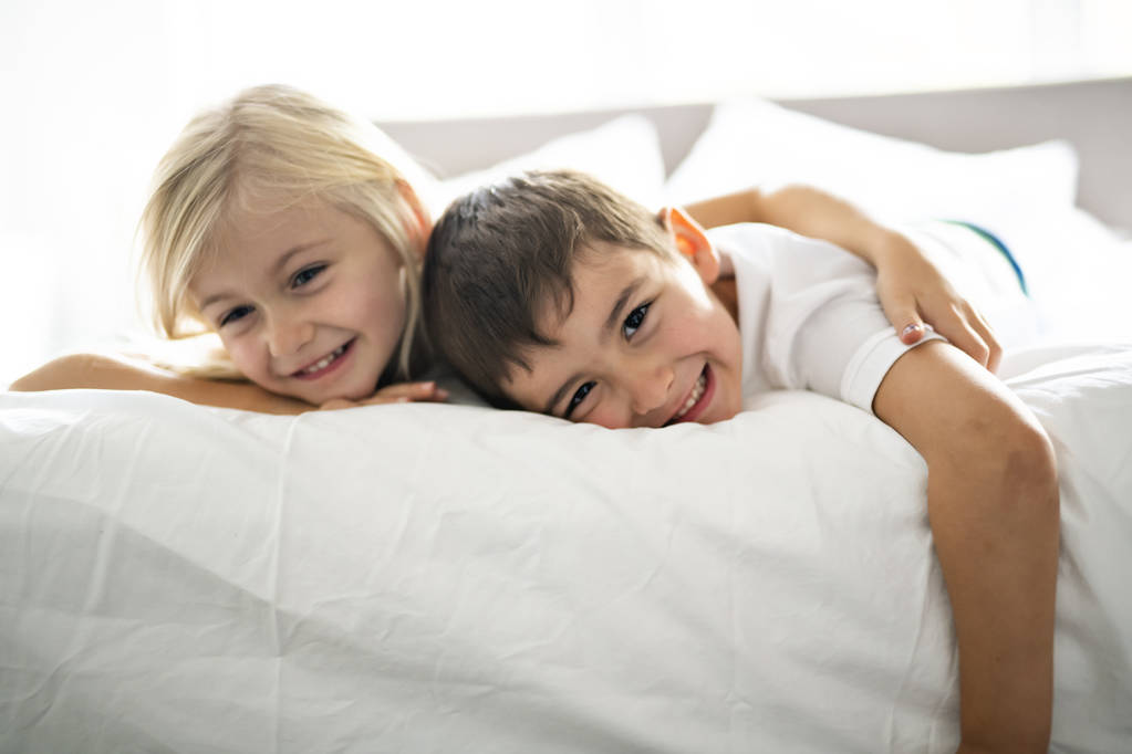 Portret szczęśliwy rodzeństwo leżącego pod koc na łóżko w sypialni w domu - Zdjęcie, obraz