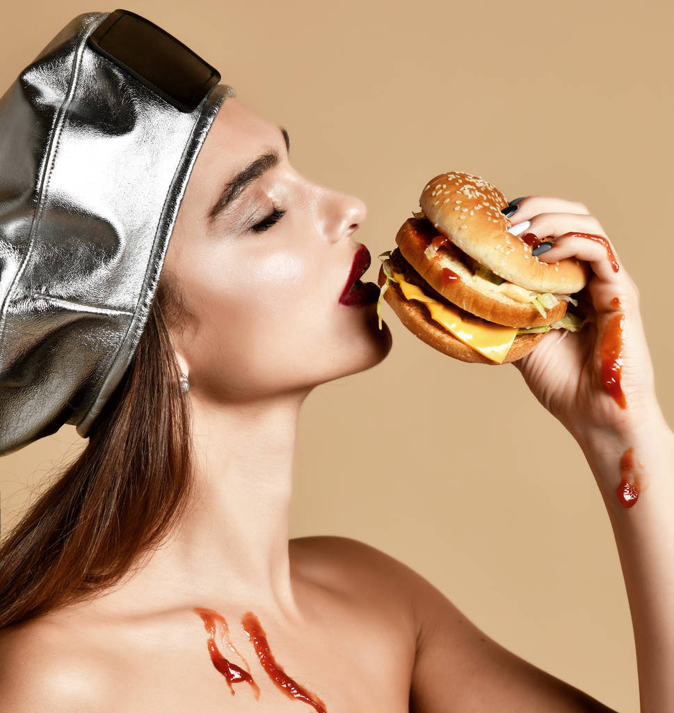 Женщина держит сэндвич с кетчупом с голодным ртом на светло-коричневом фоне
 - Фото, изображение