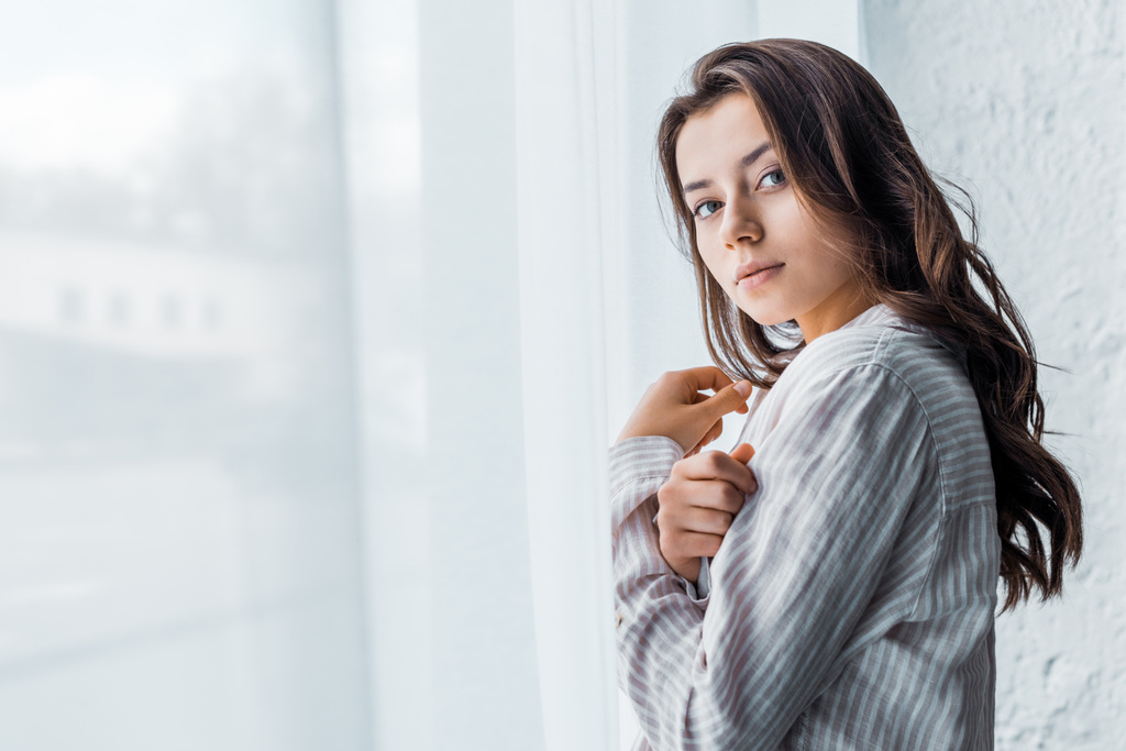 привлекательная нежная девушка в пижаме, стоящая у окна с белым занавесом
  - Фото, изображение