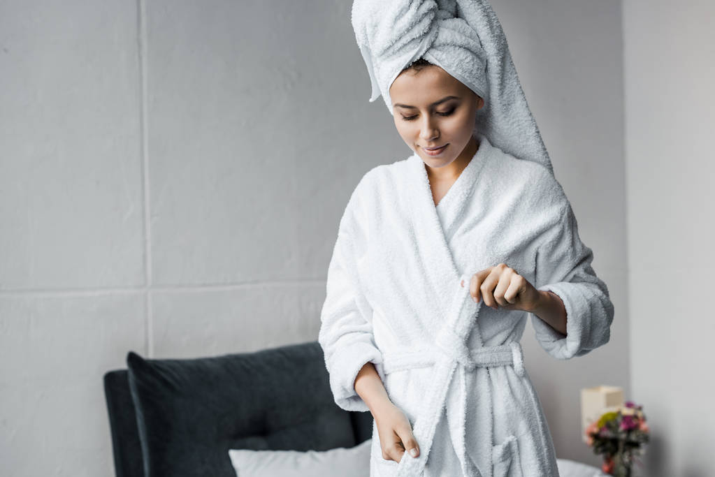 Atrakcyjna dziewczyna uśmiechający się w biały ręcznik na głowę na sobie szlafrok w sypialni - Zdjęcie, obraz