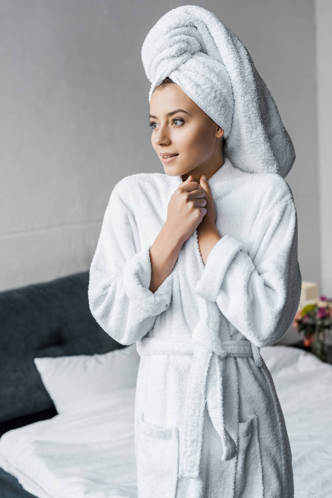 attractive dreamy girl in white bathrobe standing in bedroom - Photo, Image