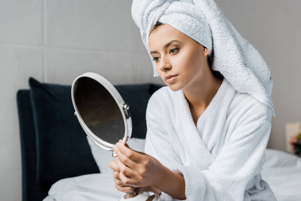 όμορφη γυναίκα στο λευκό μπουρνούζι και πετσέτα κοιτάζοντας στον καθρέφτη    - Φωτογραφία, εικόνα