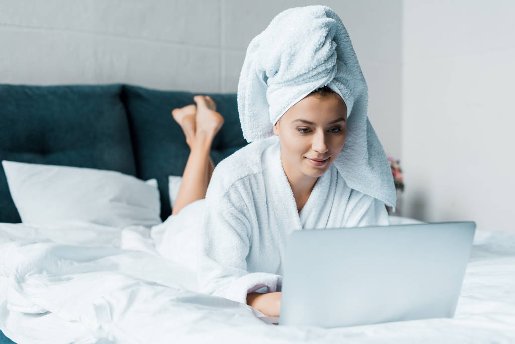 朝のベッドの上に横たわっている間ノート パソコンを使用してのバスローブの美しい若い女性 - 写真・画像
