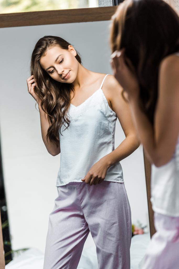 счастливая брюнетка в пижаме смотрит на свое отражение в зеркале
 - Фото, изображение