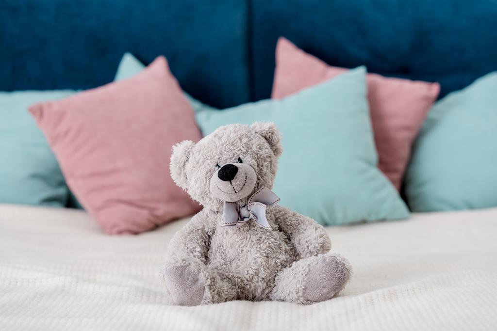 αρκουδάκι που κάθεται στο κρεβάτι με τα μαξιλάρια σε φόντο - Φωτογραφία, εικόνα