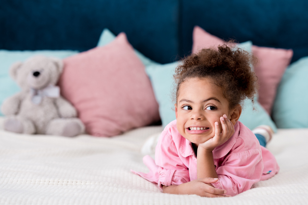 Rozkošný kudrnaté africké americké dítě ležící na posteli a usmívá se - Fotografie, Obrázek