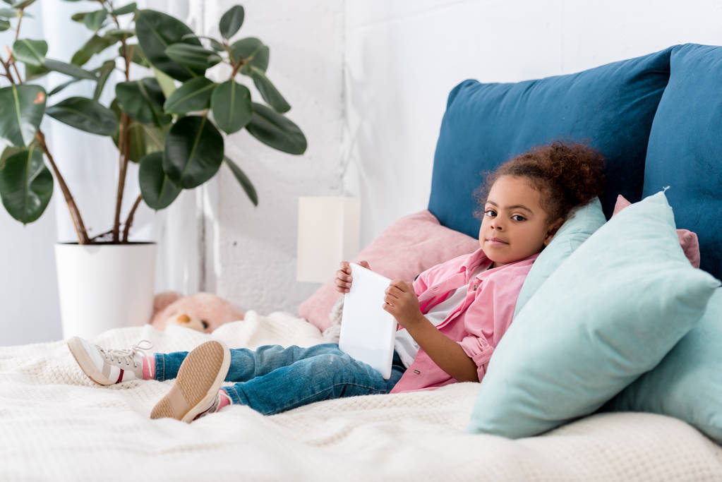 デジタル タブレットをベッドに横たわってかわいいアフリカ系アメリカ人子供 - 写真・画像
