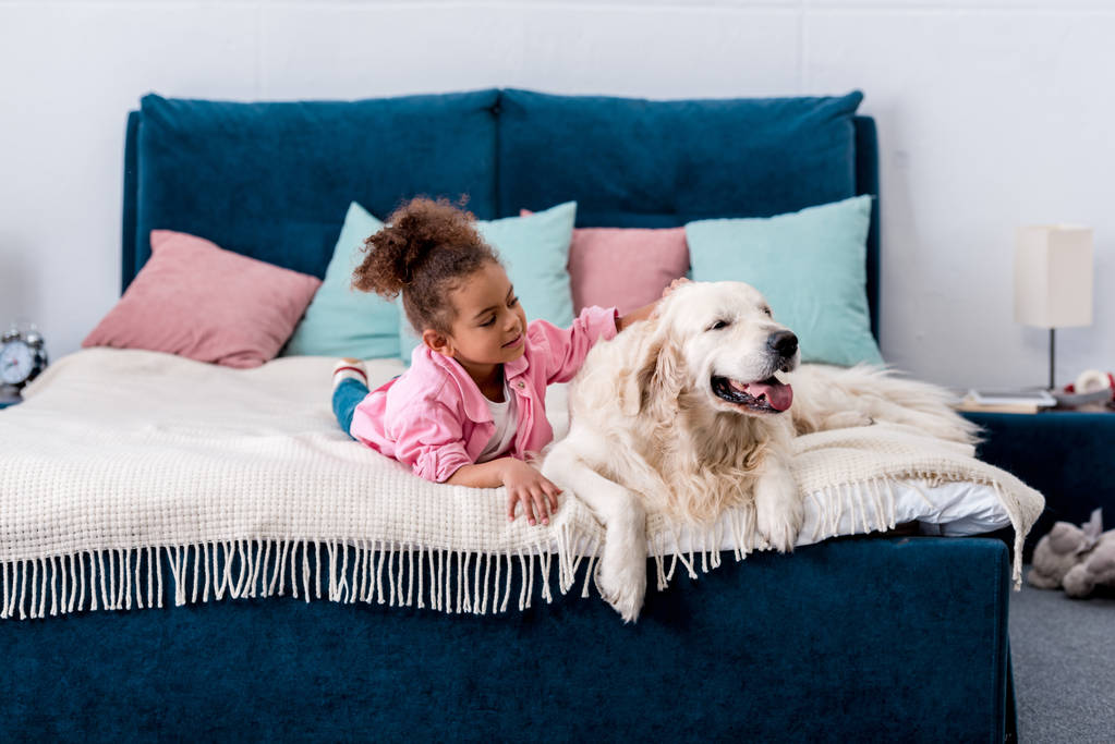 Imádnivaló afro-amerikai gyermeket az ágyon, és vakarja a hátán egy kutya - Fotó, kép