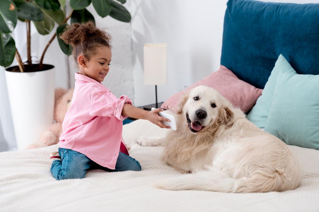 愛らしいアフリカ系アメリカ人子供の犬にベッドやショー スマート フォンの画面の上に座って - 写真・画像