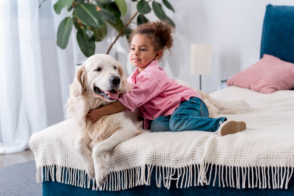 Yatakta oturmuş ve köpeğini sarılma güzel bir Afro-Amerikan çocuk - Fotoğraf, Görsel