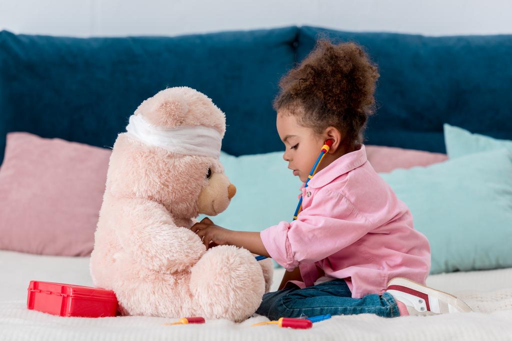 Pembe ceket Doktor oyuncak ayı ile oynayan küçük Afro-Amerikan çocuk  - Fotoğraf, Görsel