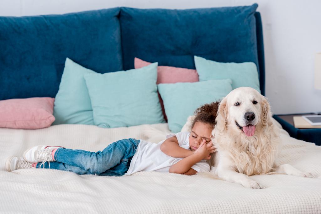 Carino bambino africano americano sdraiato sul letto e appoggiato al cane
 - Foto, immagini
