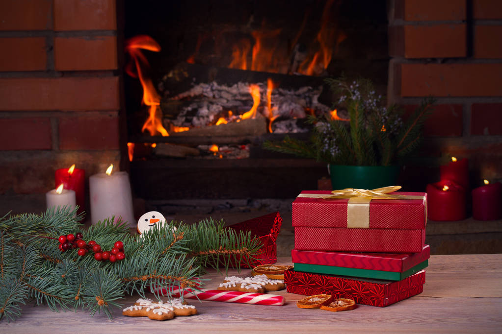 Ozdoby świąteczne, prezenty i cookies na drewnianym stole obok przytulny otwarty kominek. Zimowe wakacje koncepcja - Zdjęcie, obraz