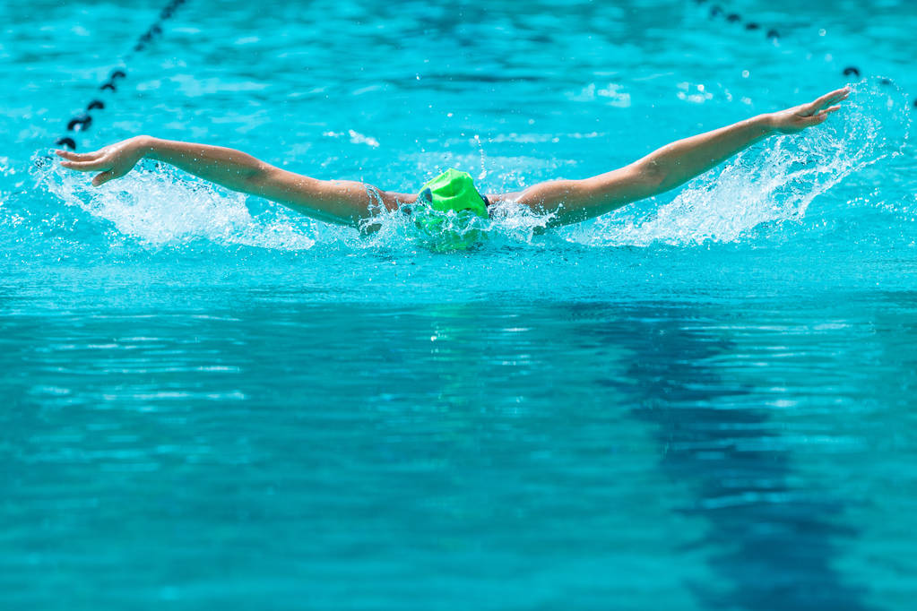 Zwemster bezig haar vlinderslag zwemmen bij een lokale zwembad op een zonnige dag, met kopie ruimte - Foto, afbeelding