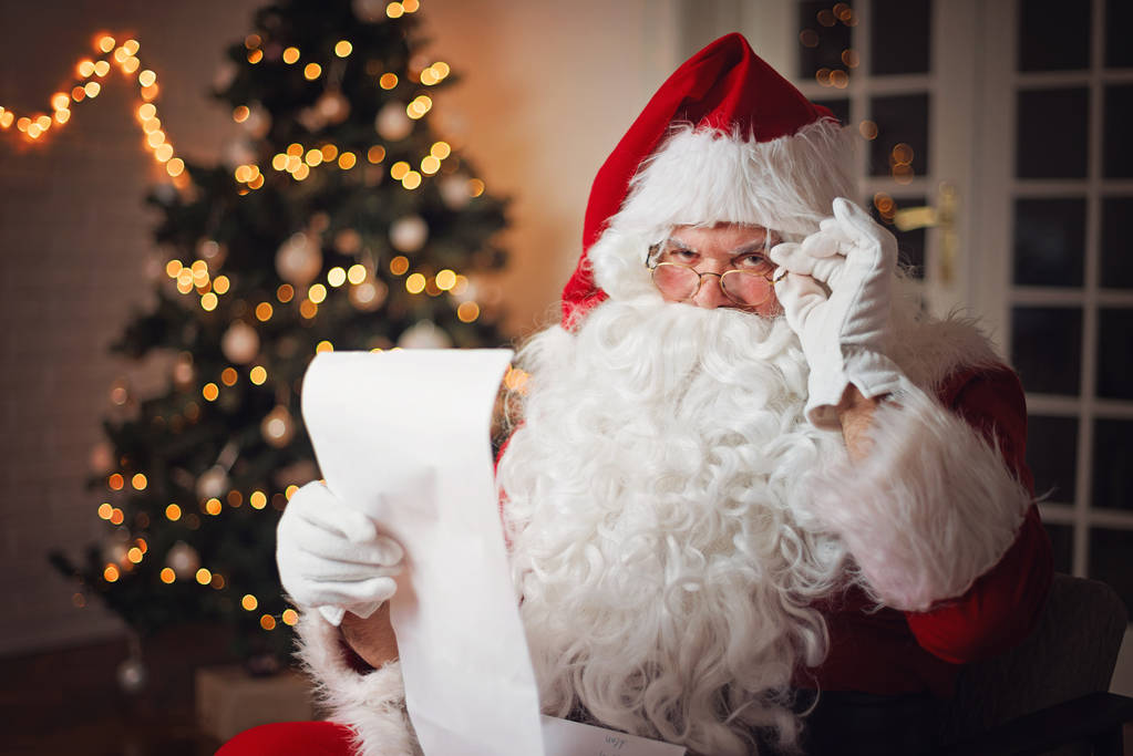 Père Noël lisant une longue liste, dans une chambre confortable
   - Photo, image