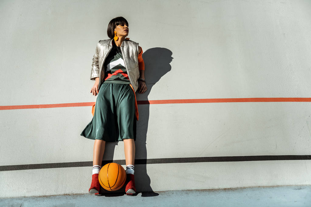 Schattig mager meisje verblijf tegen de muur met bal tussen haar benen - Foto, afbeelding