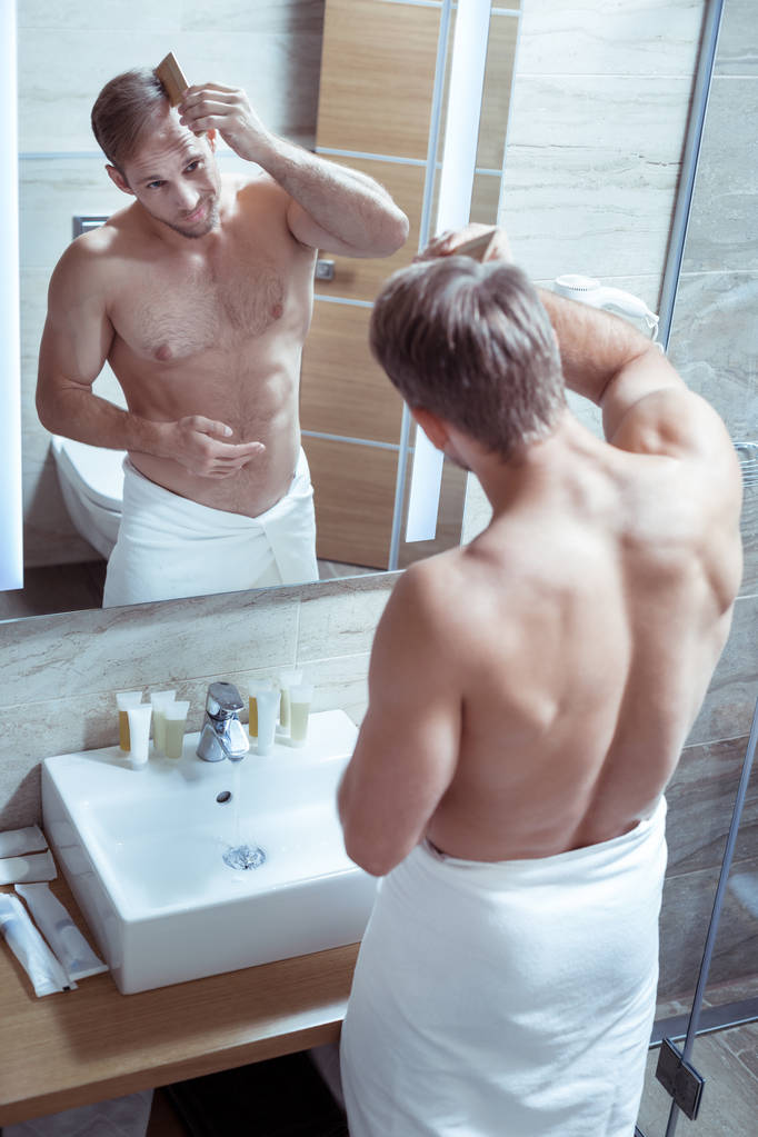 Parrakas komea mies, jolla on mukava lihaksikas vartalo kampaamassa hiuksiaan
 - Valokuva, kuva