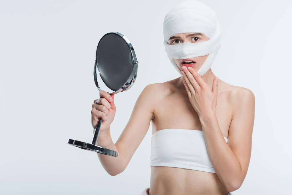 frightened woman with bandages holding mirror isolated on white - Photo, Image