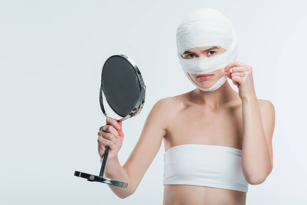 Verärgerte Frau mit Verbänden und Spiegelberührung Wange isoliert auf weiß - Foto, Bild