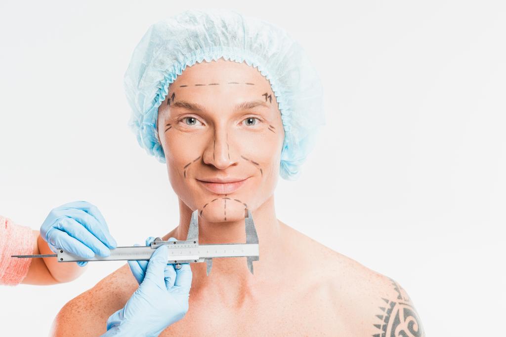 Arzt misst das Gesicht des Mannes mit gezeichneten Spuren isoliert auf weißem Grund - Foto, Bild