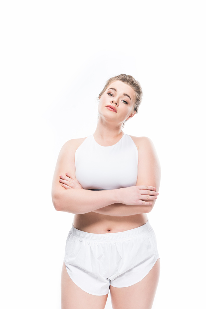 junge übergewichtige Frau in Sportkleidung, die mit verschränkten Armen steht und isoliert auf weiß in die Kamera schaut  - Foto, Bild