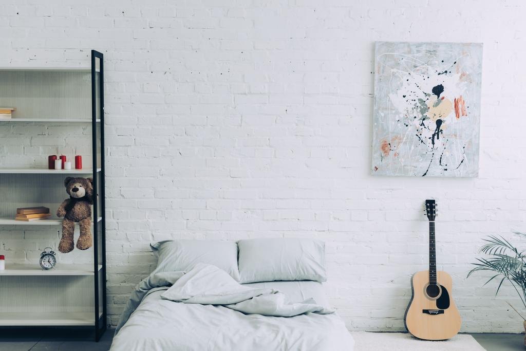 Hochwinkelblick auf modernes Schlafzimmer mit Regalen, Gitarre und Malerei an weißer Ziegelwand  - Foto, Bild